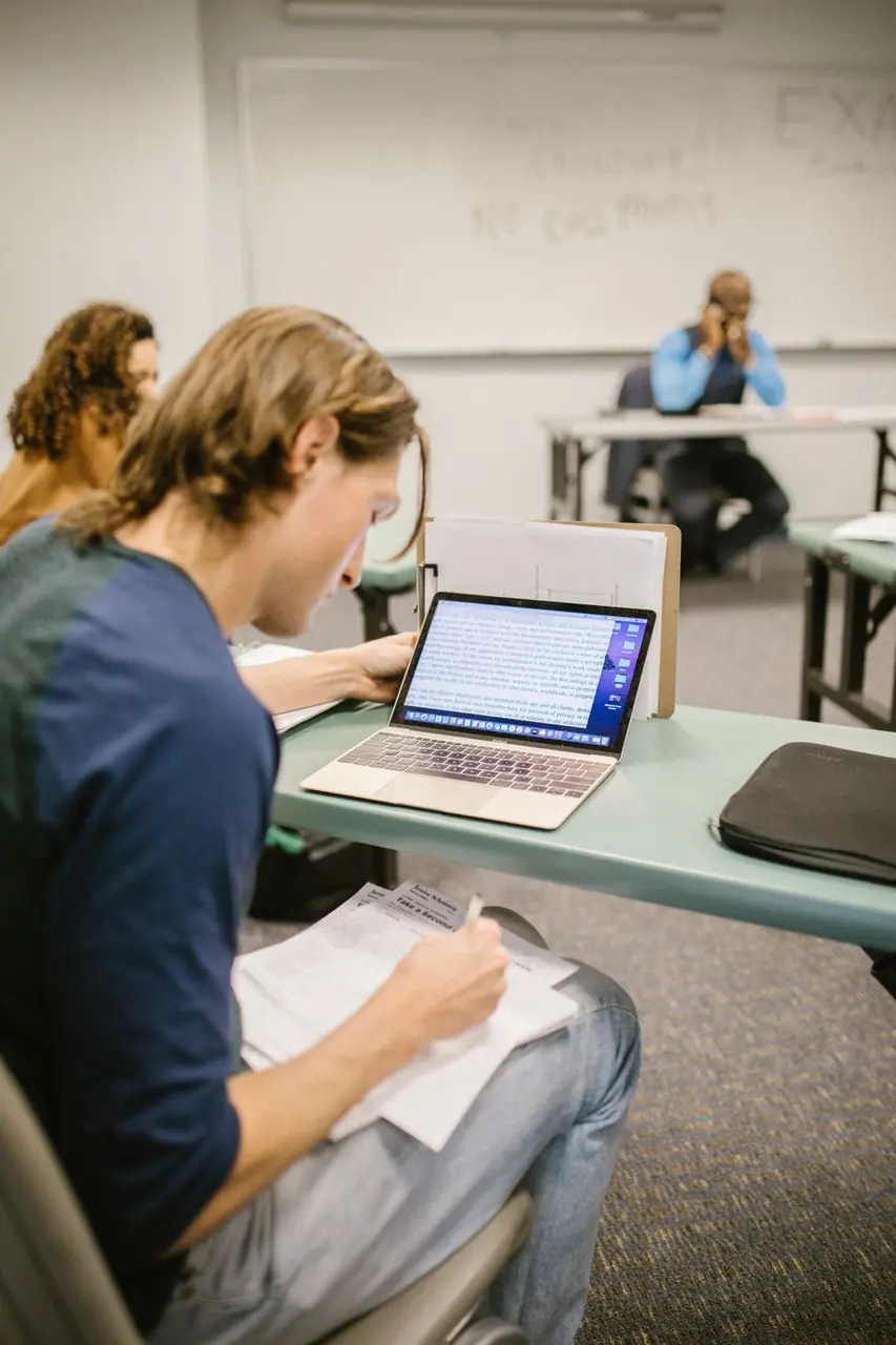 Student engaged in software problem solving on a laptop with documentation
